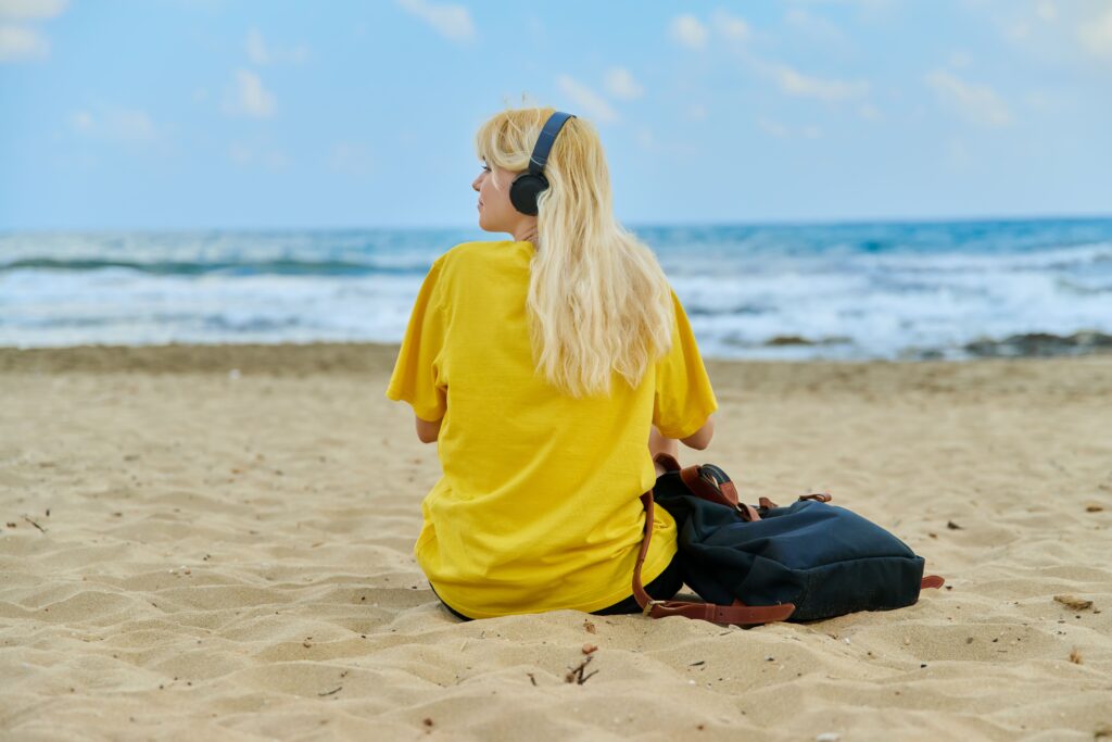 chica sentada en la playa con auriculares